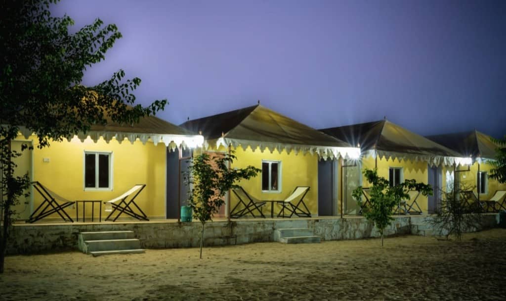 Row of illuminated yellow camp tents on the sand after dark
