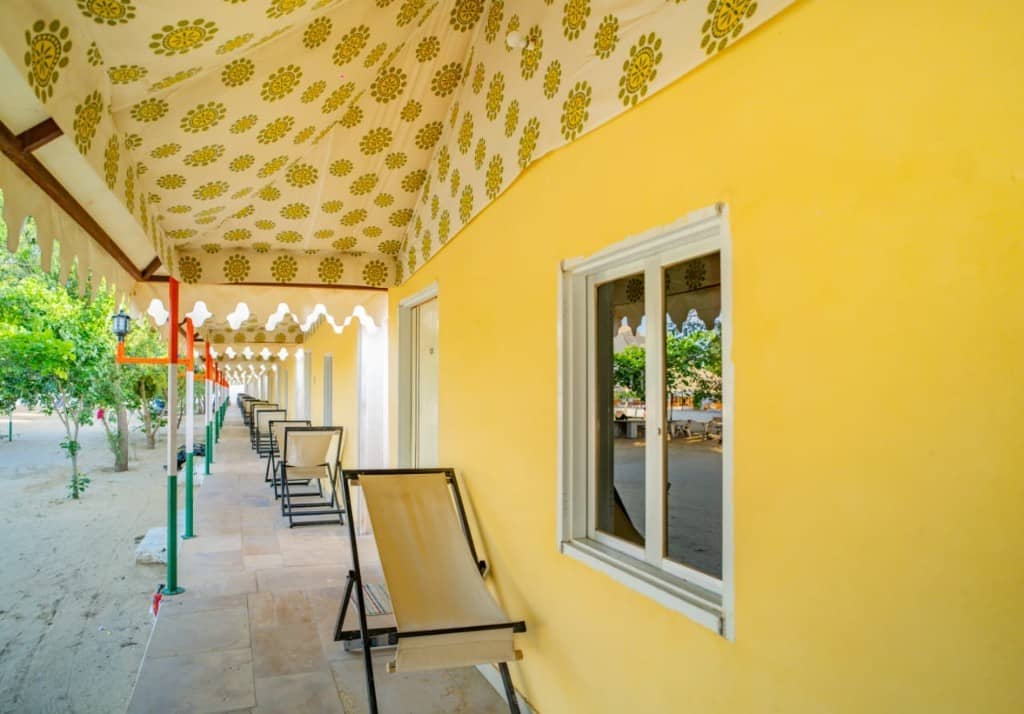 Covered walkway of yellow camp rooms with a chair outside each door