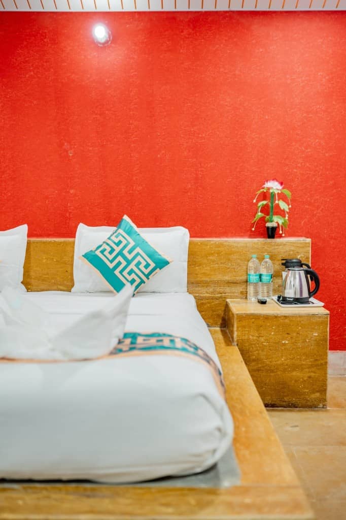 Hotel bed against a red wall with a kettle and water on the side table