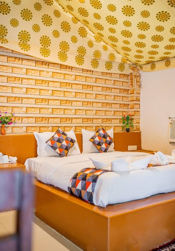 Double bed in a tent room under a patterned canvas roof and brick wall