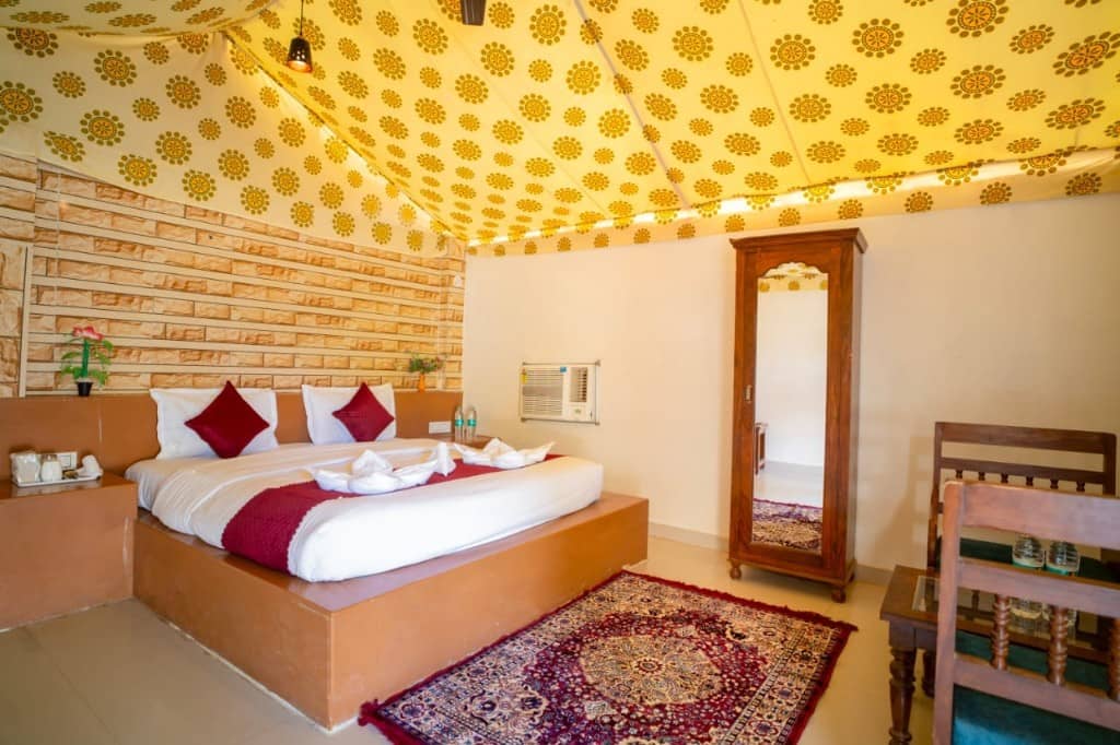 Tent bedroom with patterned cushions, a brick wall and a standing mirror