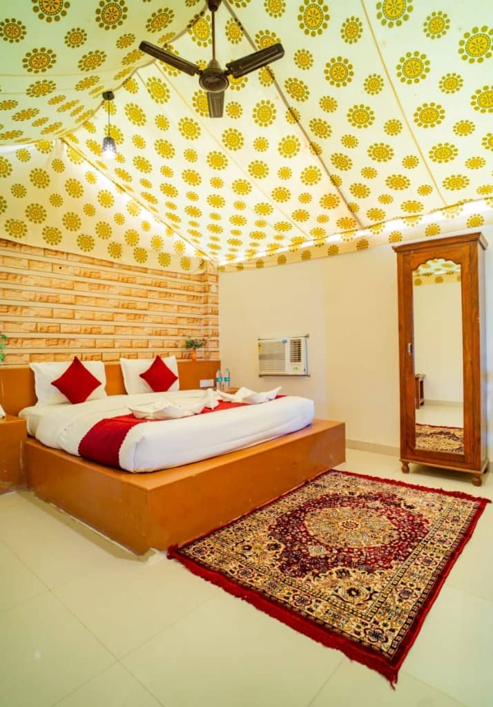 Tent room with a red bed runner, patterned rug and wooden mirror wardrobe
