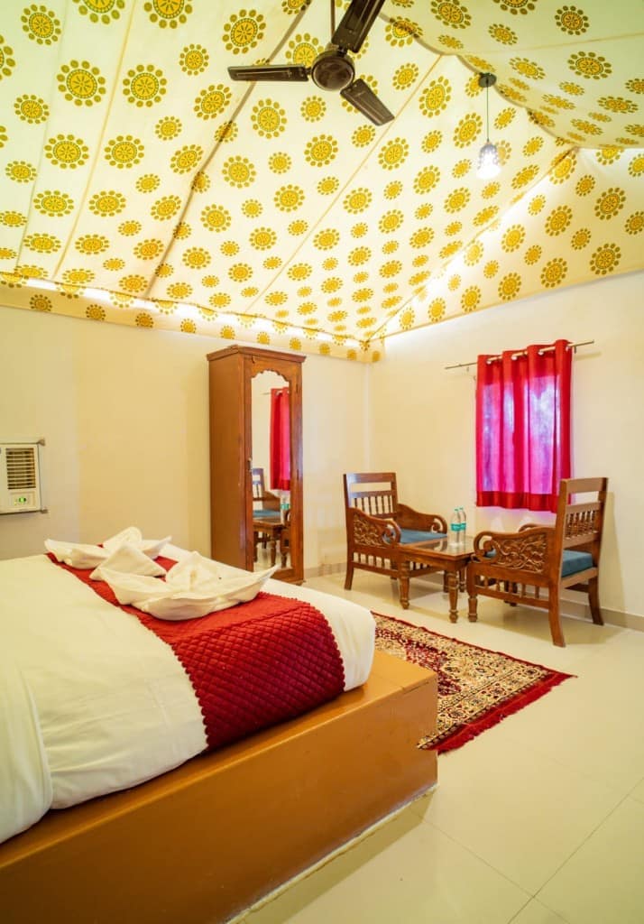 Camp tent room with a red bedspread, wooden chairs and an air cooler